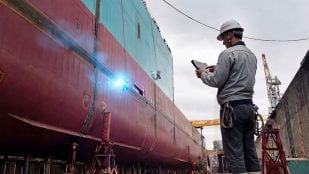 Imagen conceptual de Kawasaki, no una foto real: un robot soldador de barcos con una chispa de soldadura en el casco y un operario con una tableta