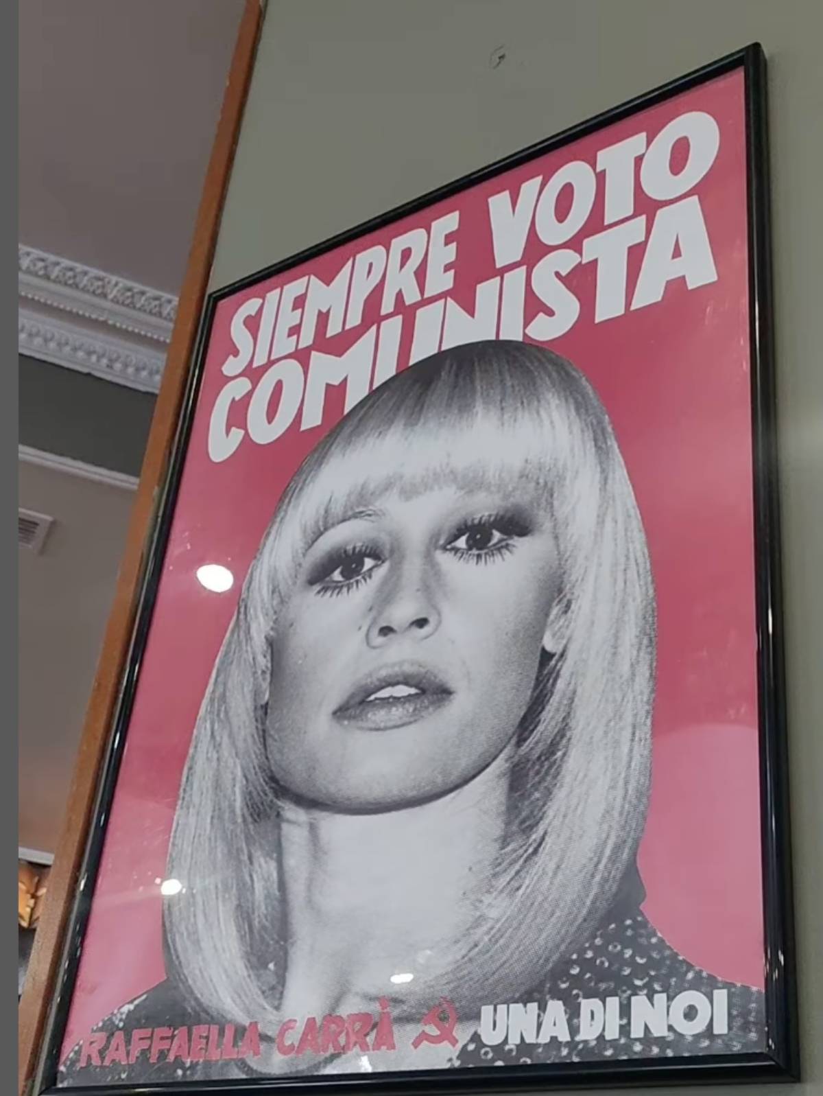 En la pared de la taberna cuelga un cartel de est&eacute;tica pop en blanco y negro y fondo rojo, con la foto de Raffaella Carr&agrave;. (Redes Sociales)
