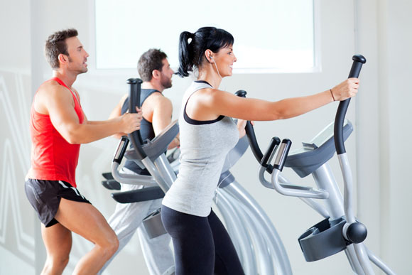 man and woman with elliptical cross trainer at gym