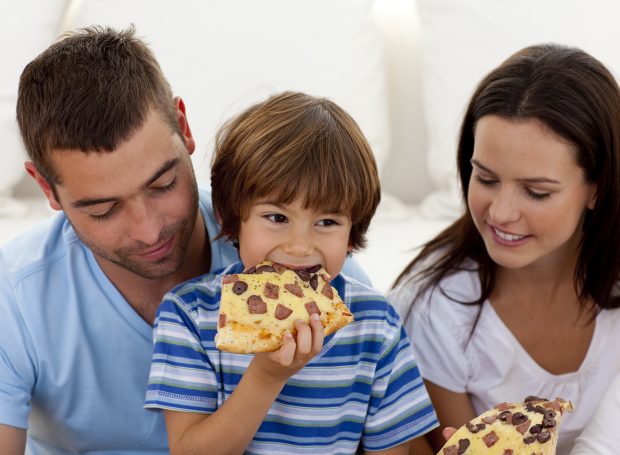 Un hijo comiendo pizza con sus padres. / Gtres