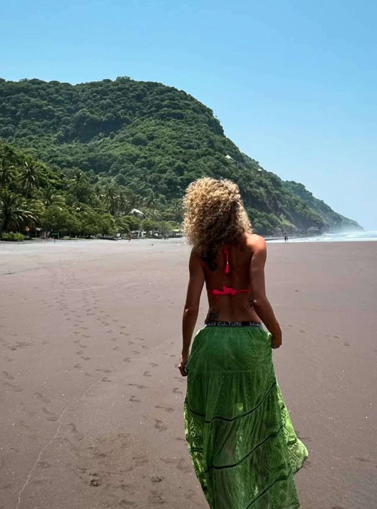 También se la ve caminando por una extensa playa de arena oscura, de espaldas. (Redes Sociales)