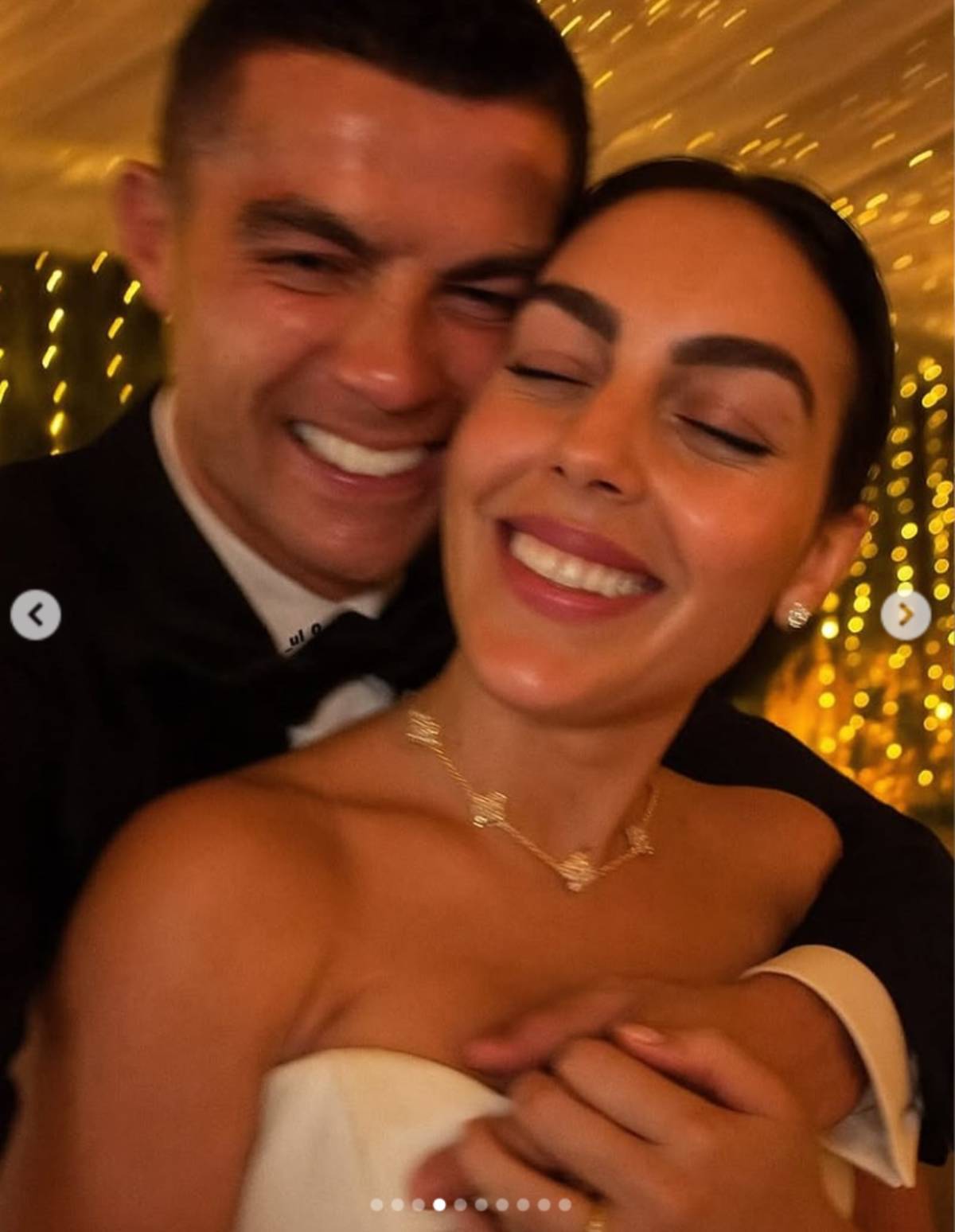 La pareja sonríe bajo el cielo abierto, con Georgina luciendo un vestido palabra de honor y collar brillante. (Creado con IA)