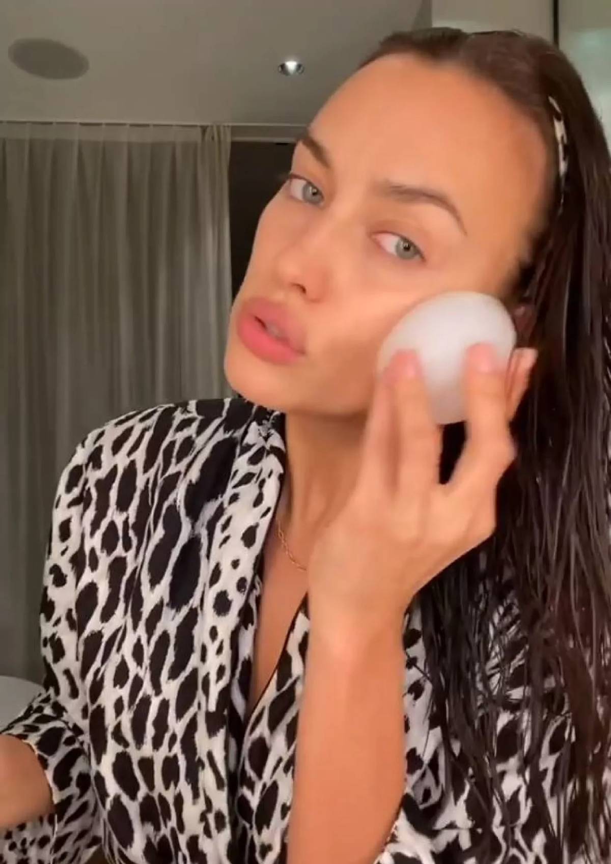 Irina Shaik posa frente a cámara aplicándose una gran bola de hielo blanca directamente sobre la mejilla.