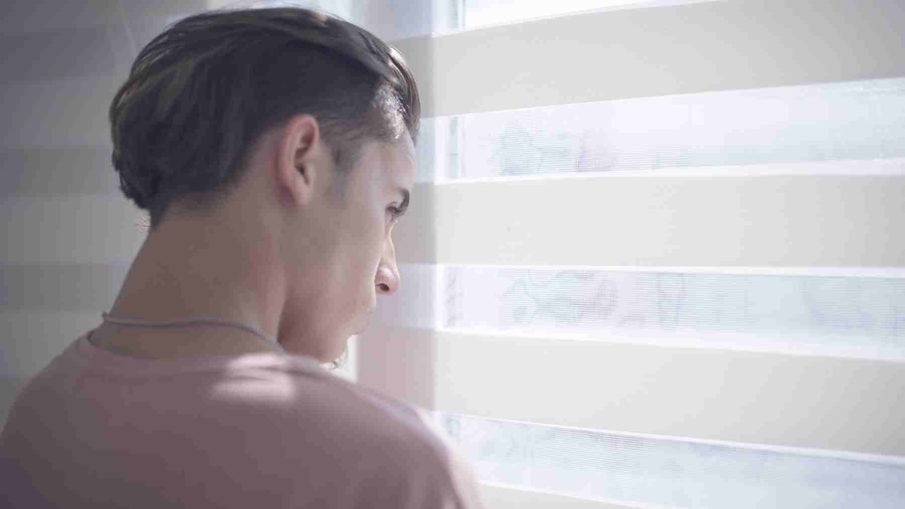 Young adult looking out a window, reflecting feelings of anxiety and uncertainty about the future