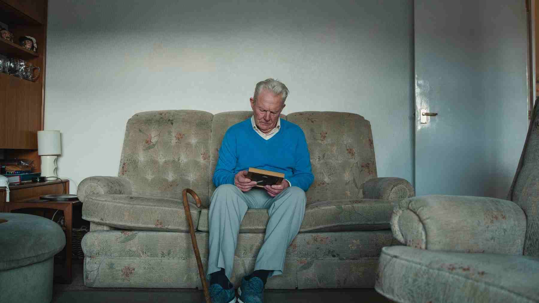 Elderly man sitting on a couch looking at an old photo, illustrating memory, aging, and brain recall