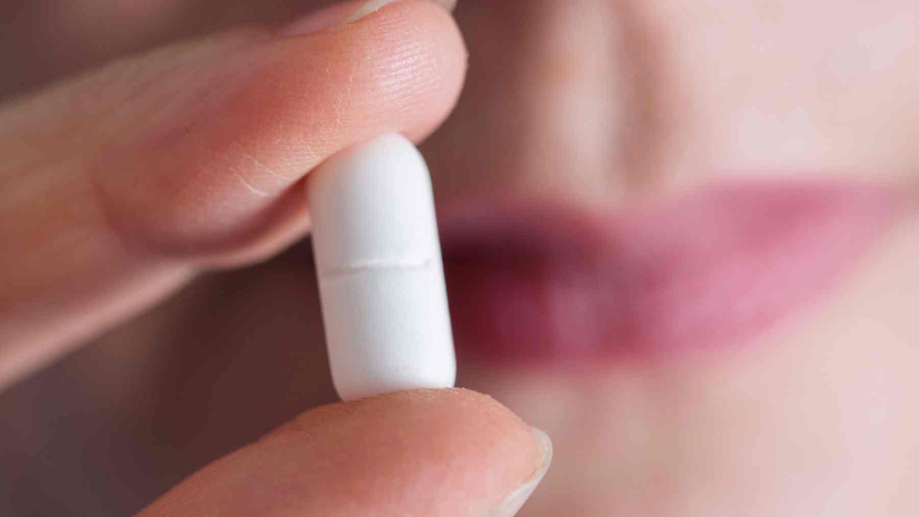 Close-up of a person holding an ibuprofen pill between fingers near their mouth
