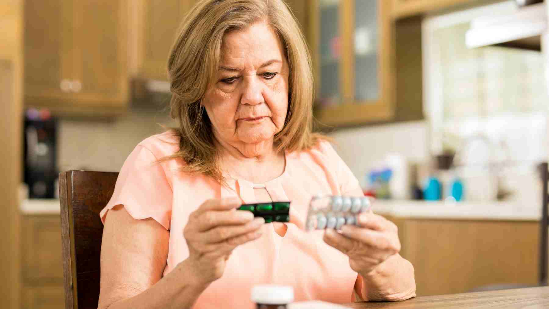 Older woman looking at blister packs of supplements at home