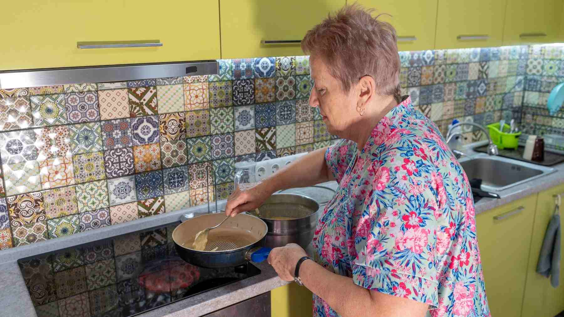 Older woman cooking in a tidy kitchen, illustrating how cleaning as you go can reduce stress, clutter, and mental fatigue