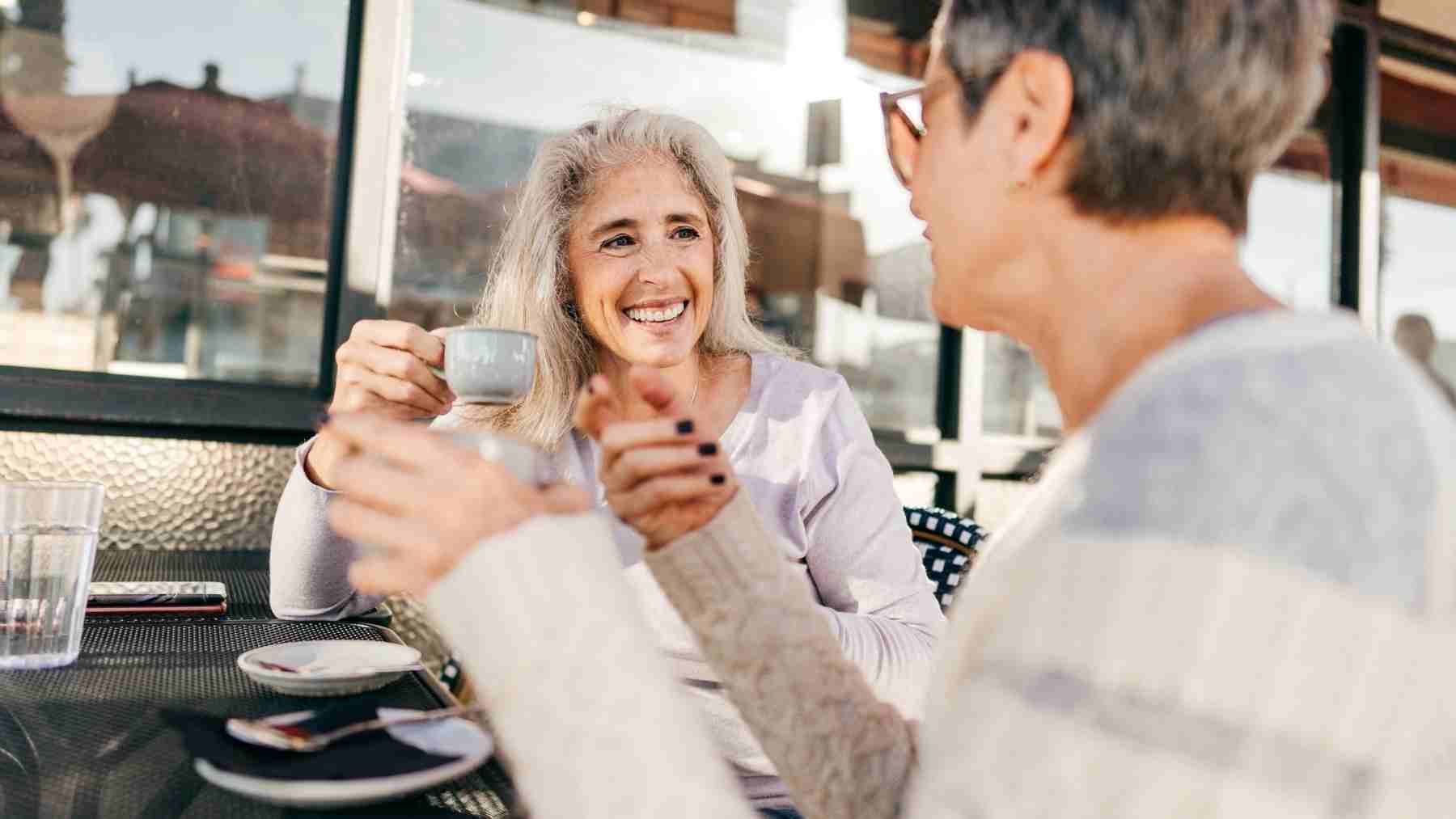 Older women smiling and talking over coffee, representing personality growth and emotional resilience after age 60