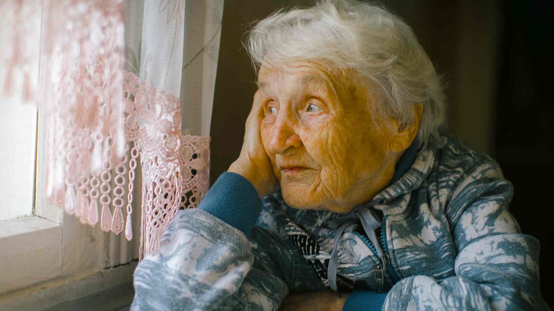 Elderly woman looking out a window as psychology research highlights how people underestimate failure and social crises