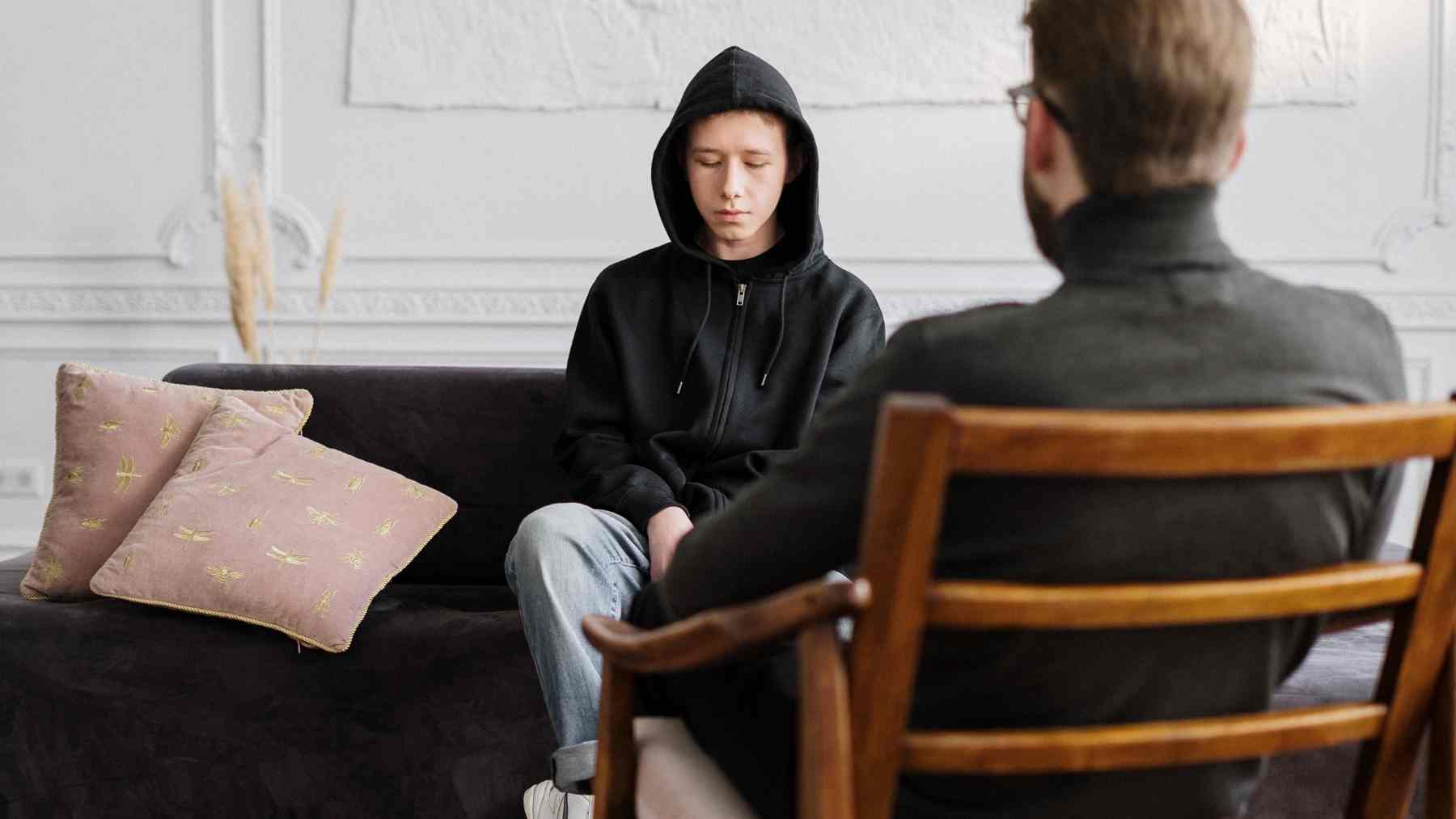 Teen in hoodie sitting silently during therapy session, reflecting loneliness despite strong social awareness