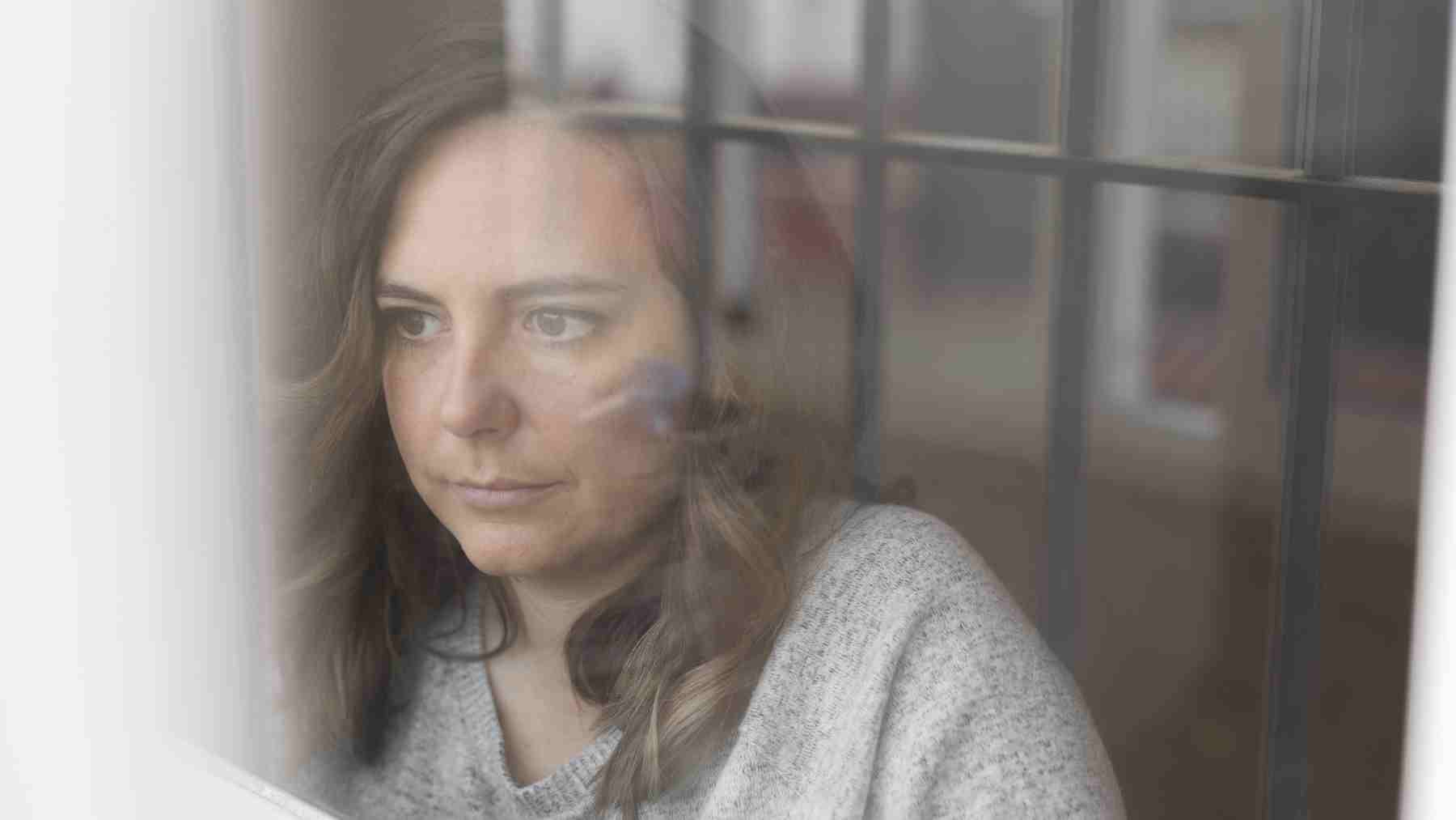 Woman looking thoughtful through a window, reflecting on emotions, compassion, and personal well-being