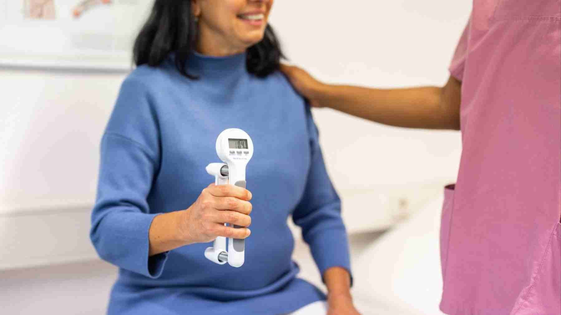 Older woman performs grip strength test with dynamometer during clinical assessment linked to longevity study