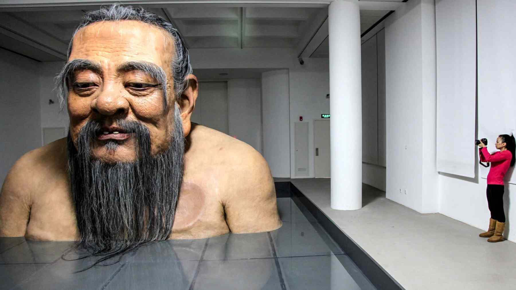 Large sculpture of Confucius inside a gallery as a visitor photographs the ancient Chinese philosopher