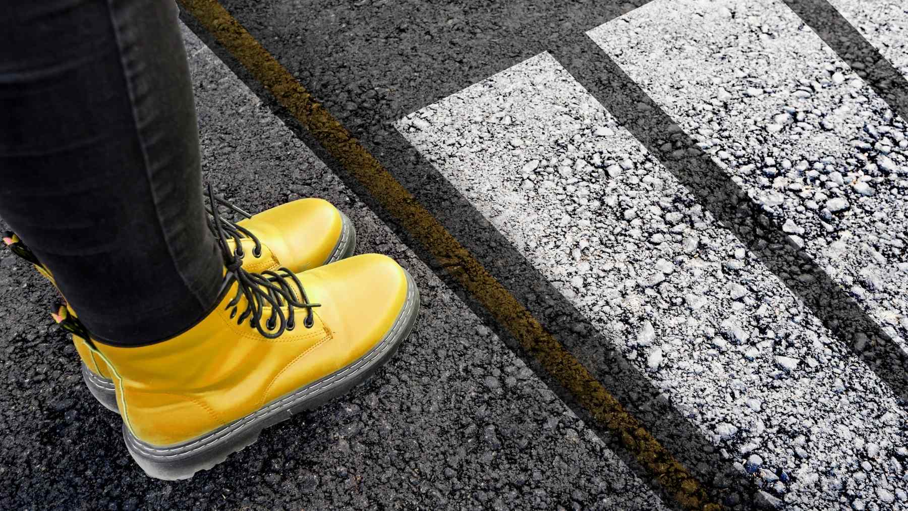 Yellow boots at a crosswalk as a pedestrian pauses before crossing, symbolizing a quick thank-you gesture and mindfulness.