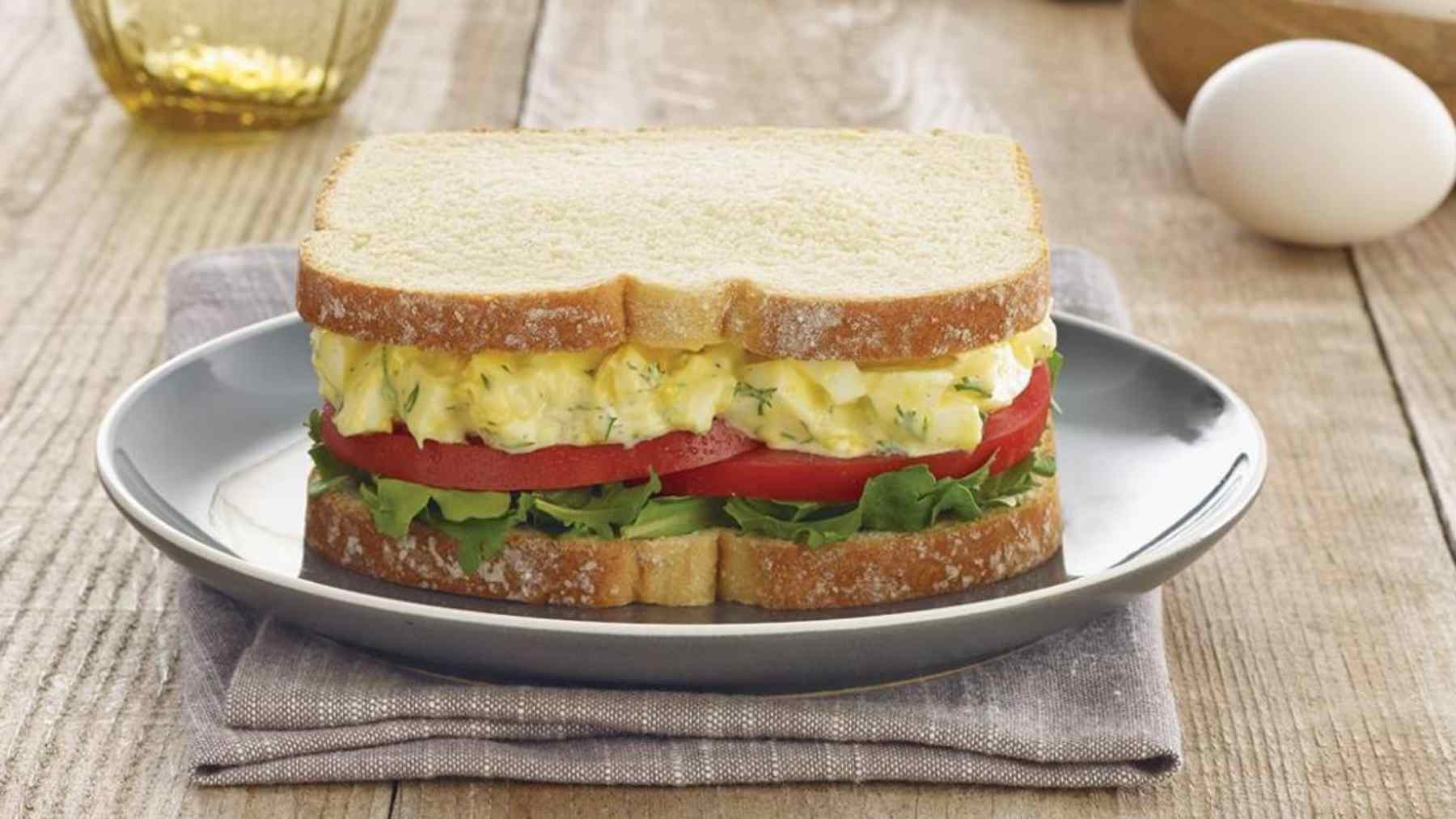 Egg sandwich with creamy filling, tomato, and lettuce on white bread served on a plate