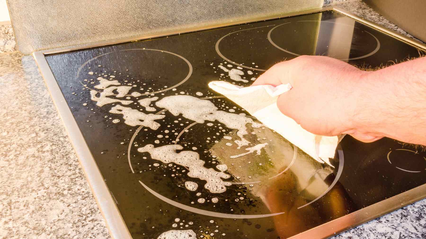 Person wiping a glass-ceramic cooktop with a paper towel to remove soap residue, streaks, and marks.