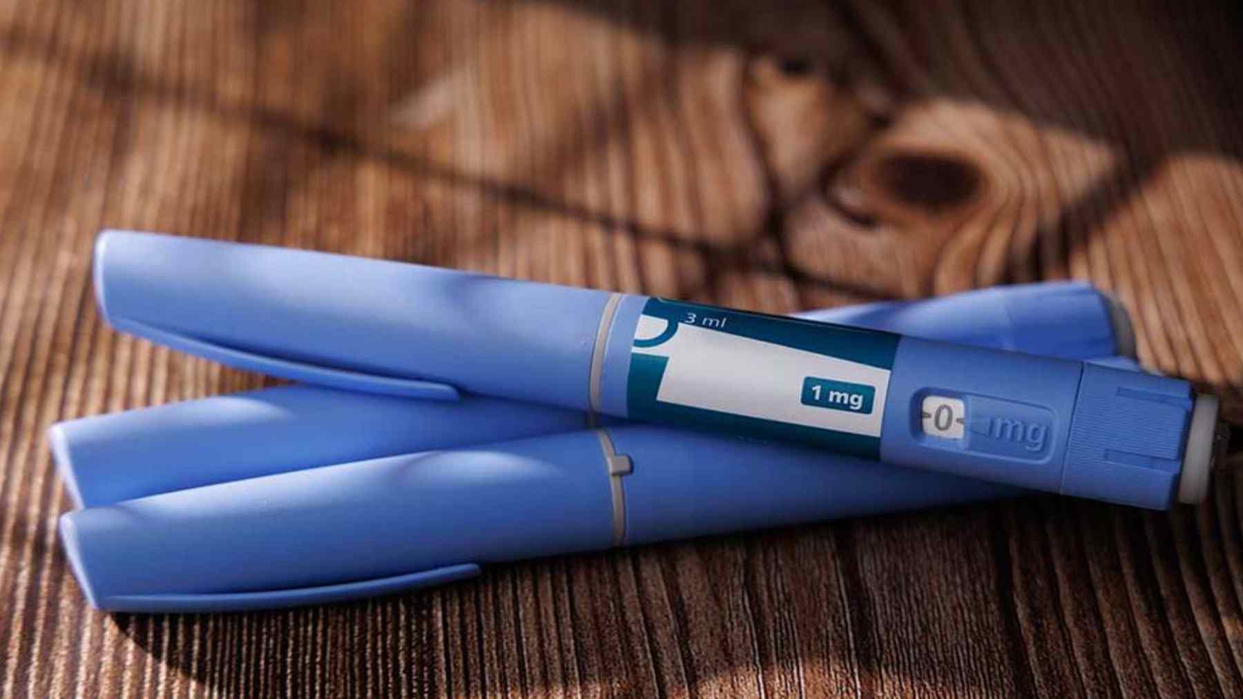 Two GLP-1 injection pens on a wooden surface, illustrating semaglutide-style weight loss medication dosing.
