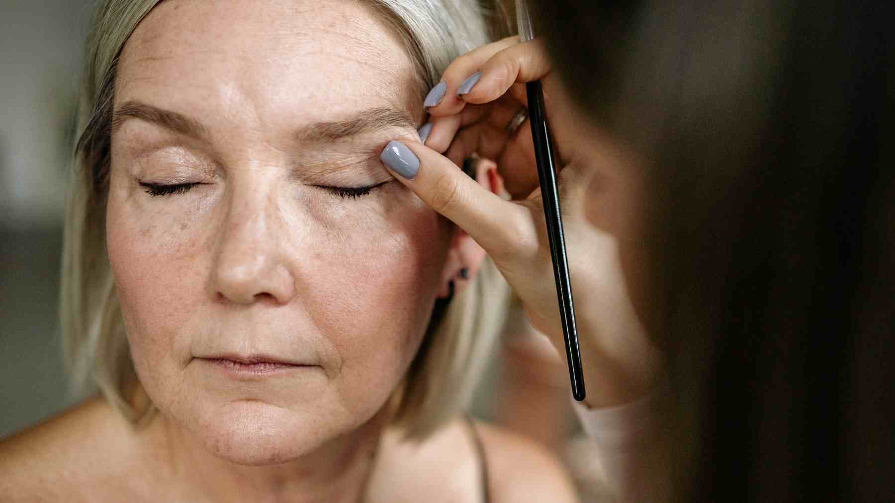 Woman having eye makeup applied, reflecting social expectations and beauty standards
