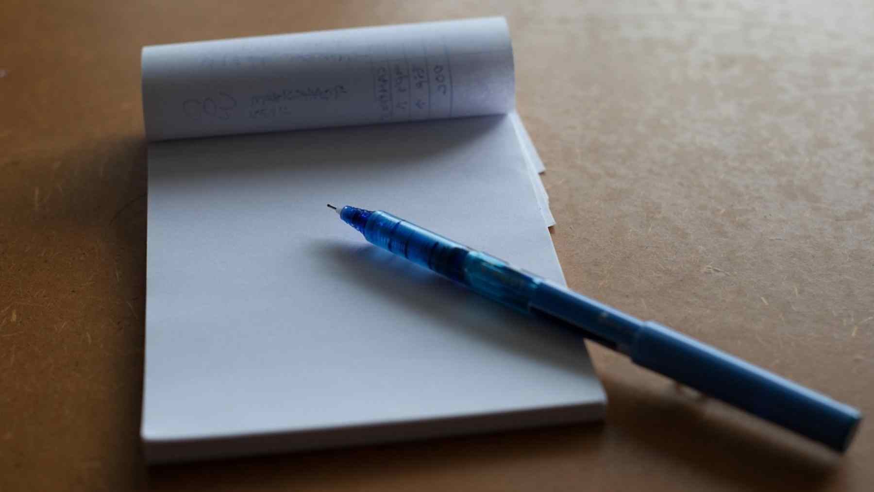 Blue pen on an open notebook, illustrating handwritten notes and focused attention during a meeting