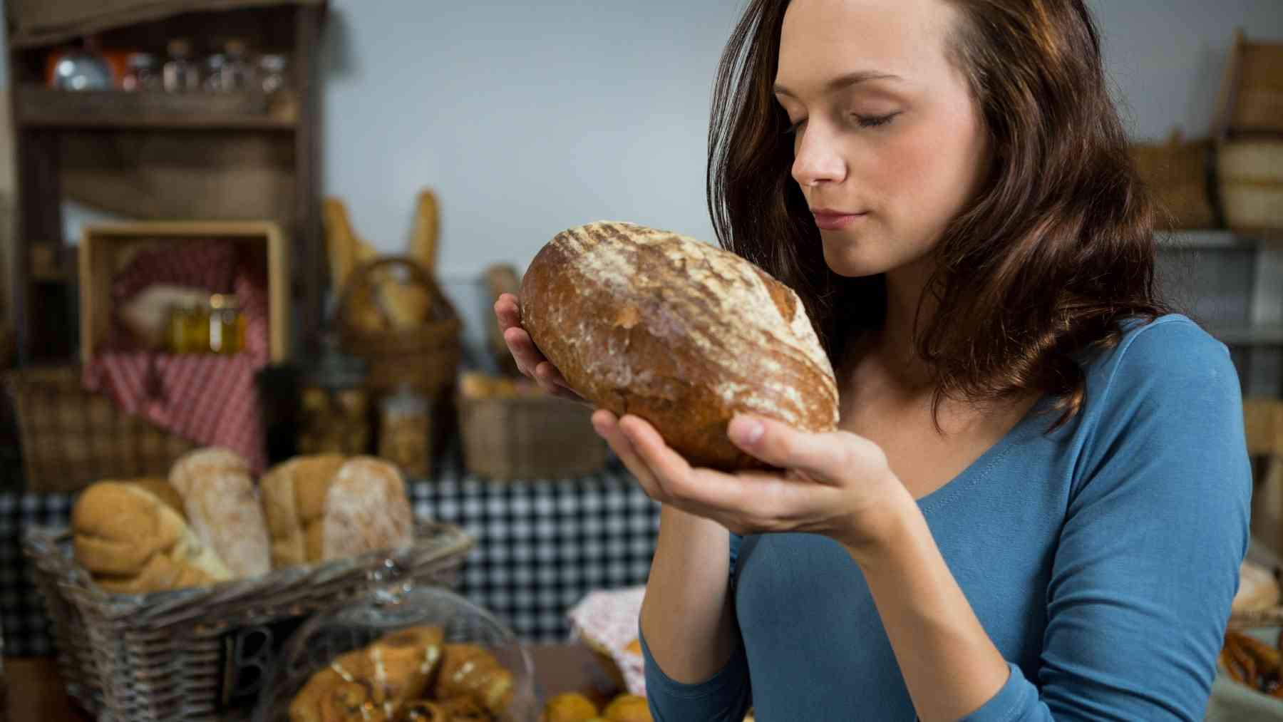 Woman holding and smelling a loaf of dark bread while learning that color does not always mean whole grain