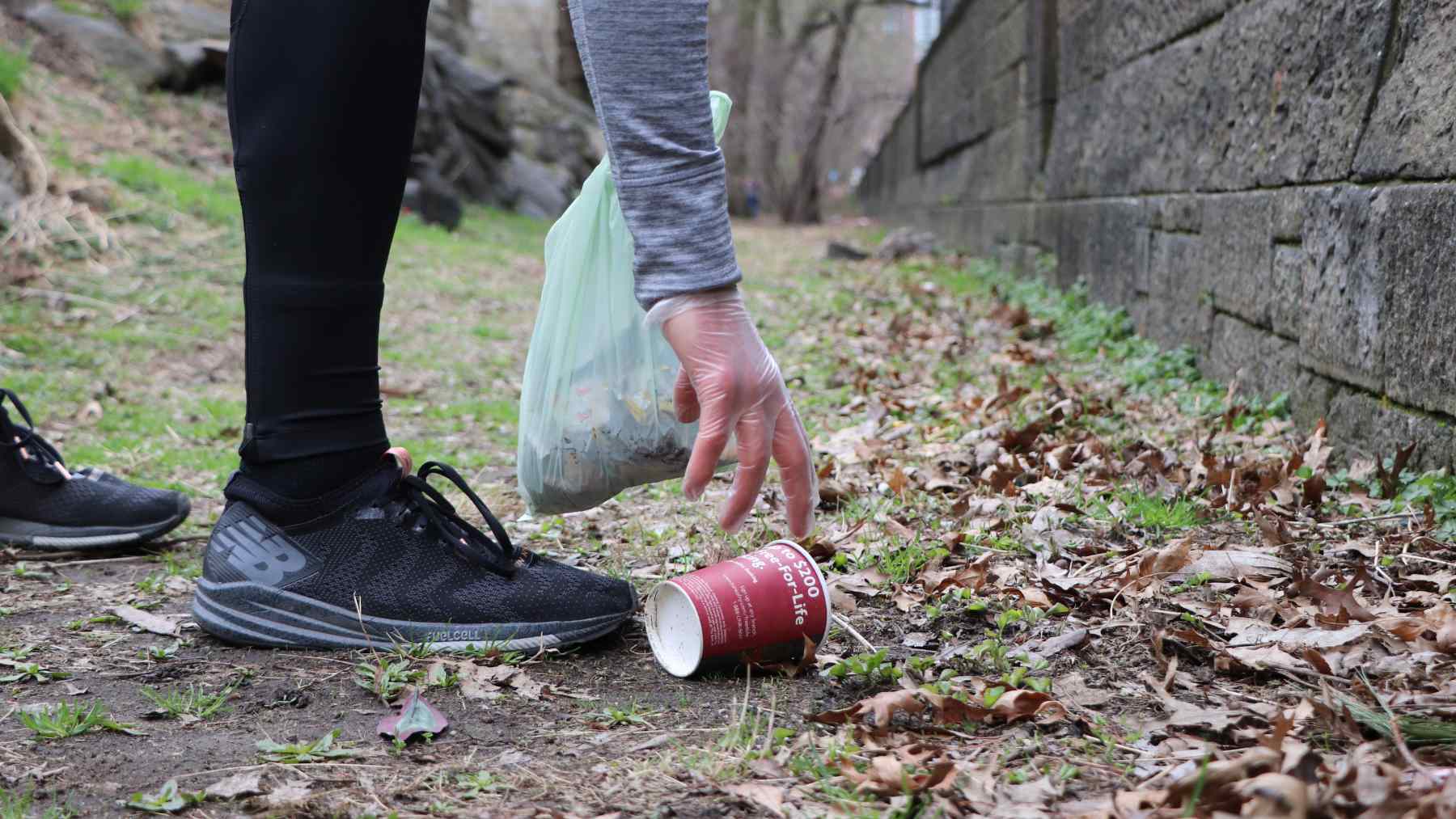 NYC runner plogging, picking up litter with a glove and trash bag during an outdoor run