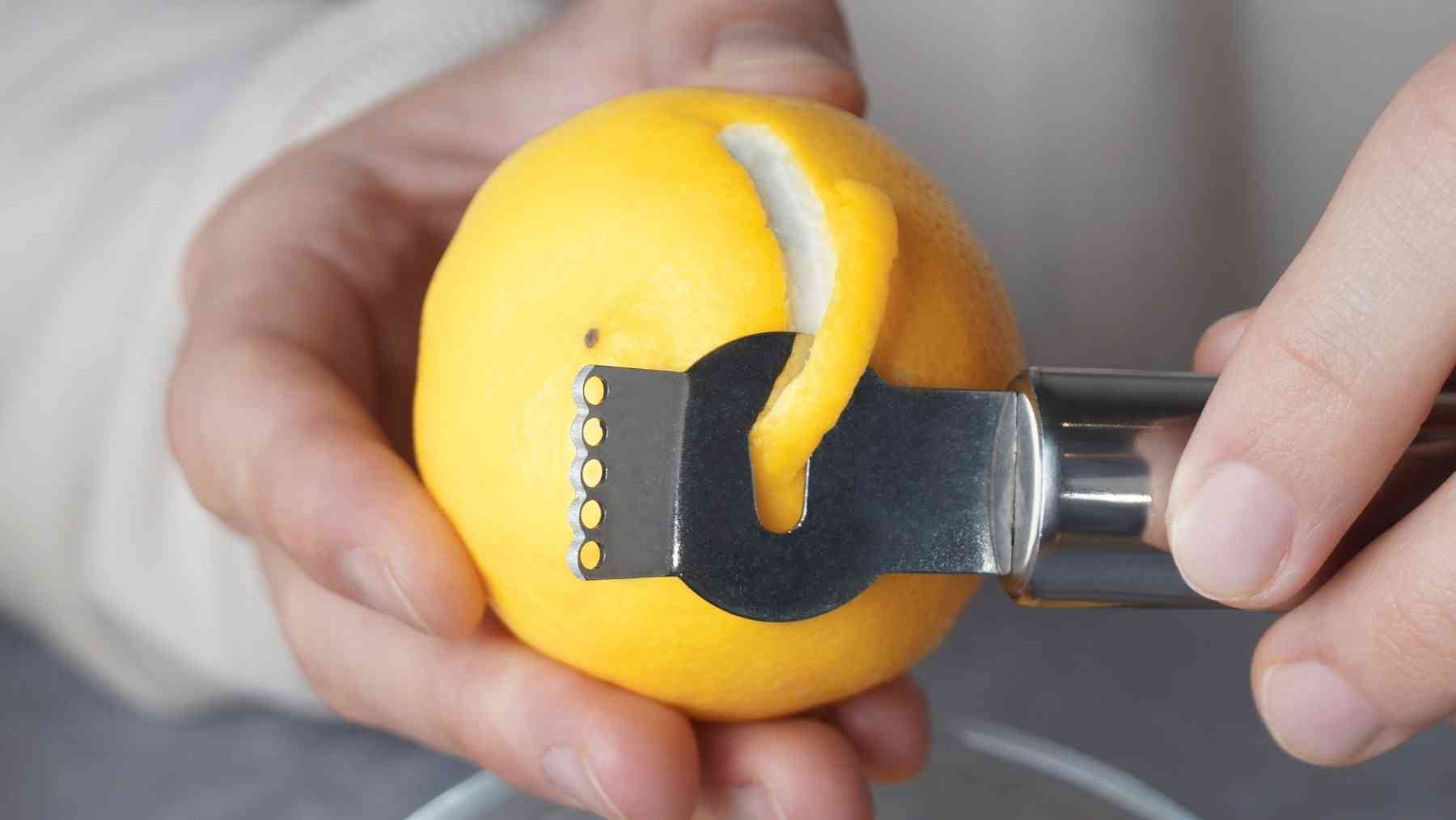 A person peeling a lemon peel with a metal citrus zester for a natural home freshening trick
