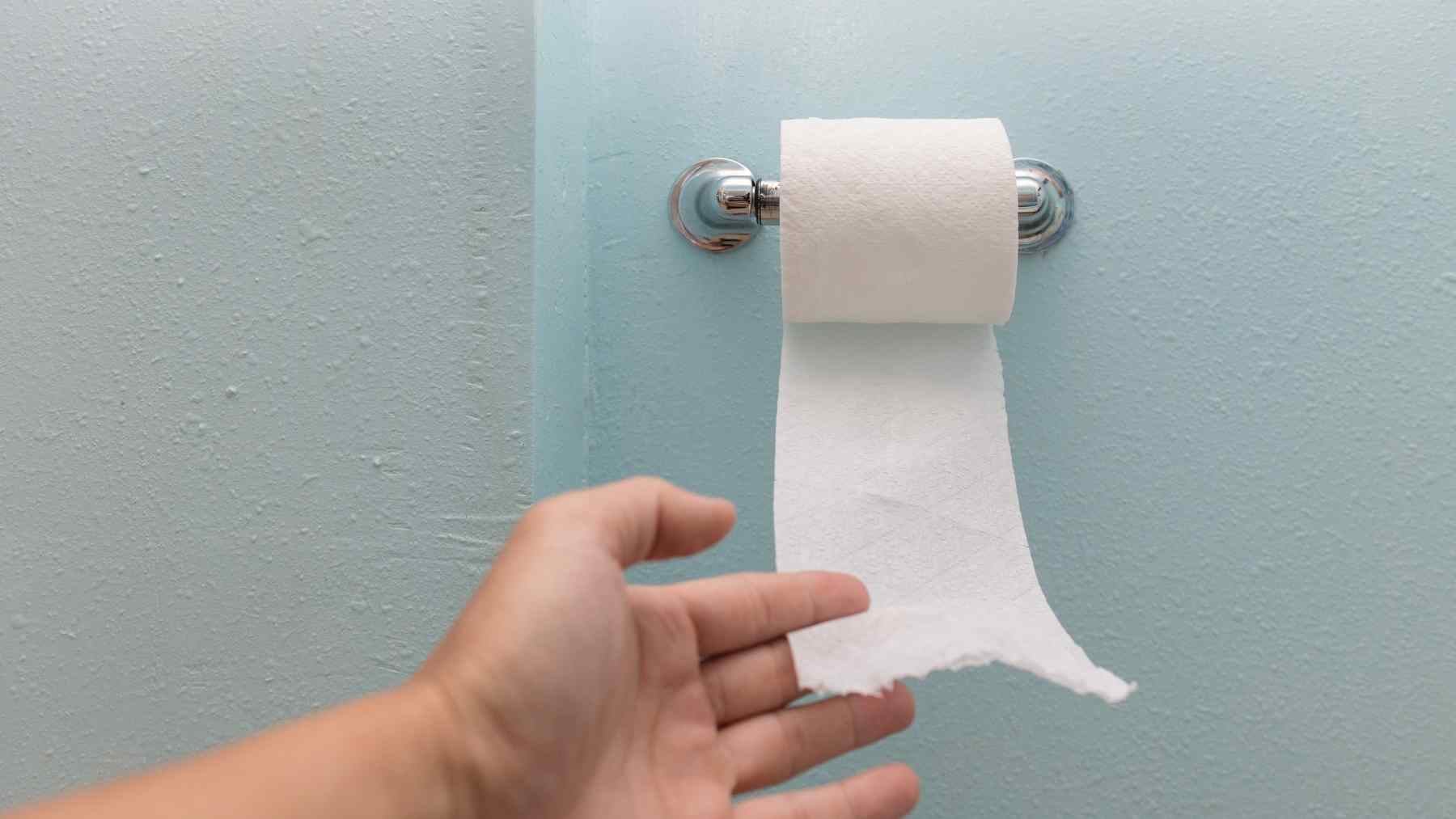 Hand reaching for toilet paper in a bathroom, illustrating a morning bowel routine recommended by gastroenterologists