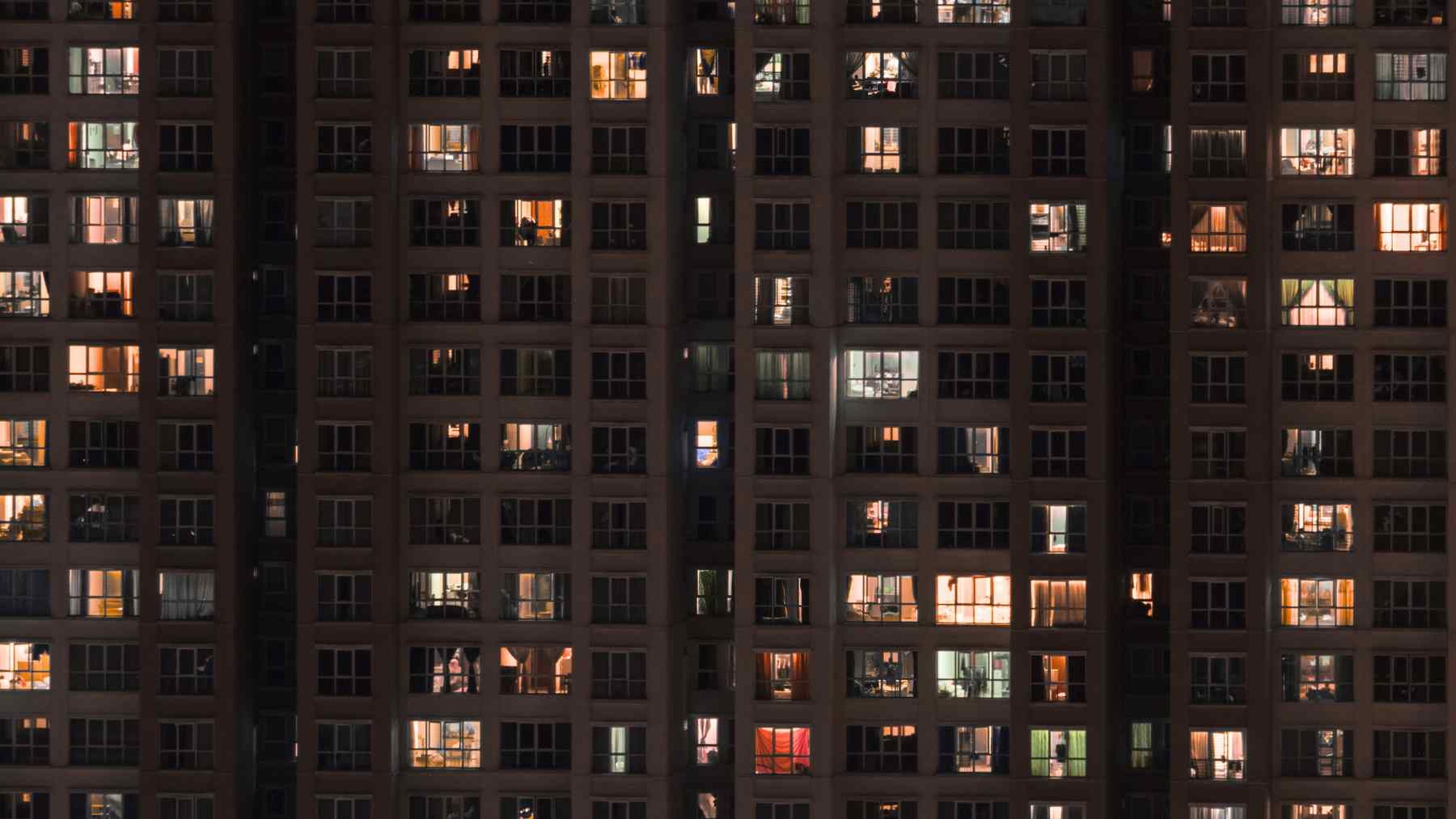 Apartment windows at night with some blinds open and warm indoor lights visible