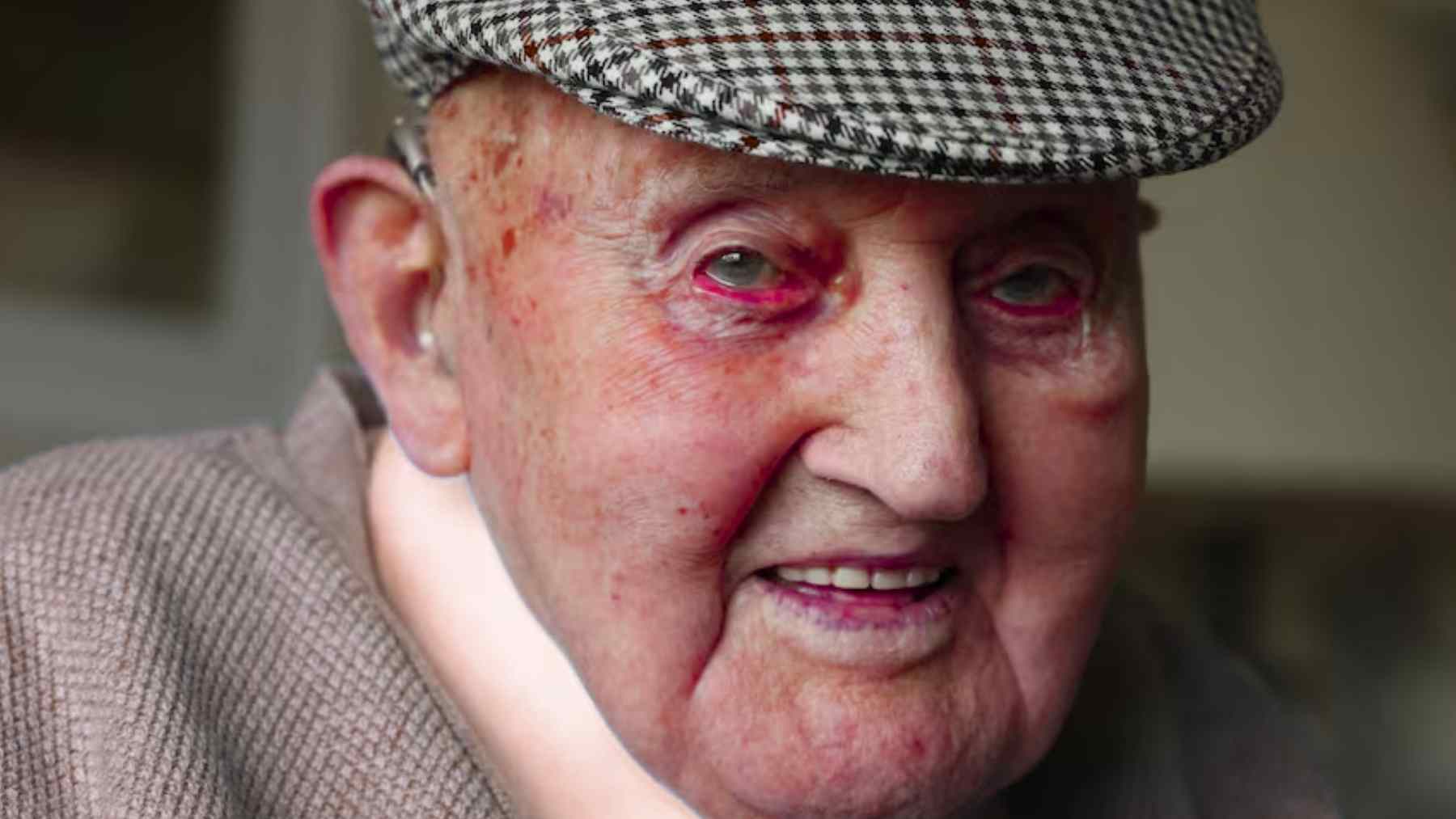 Paddy Claffey, 104, smiles at home wearing a flat cap and gray sweater in County Offaly, Ireland.