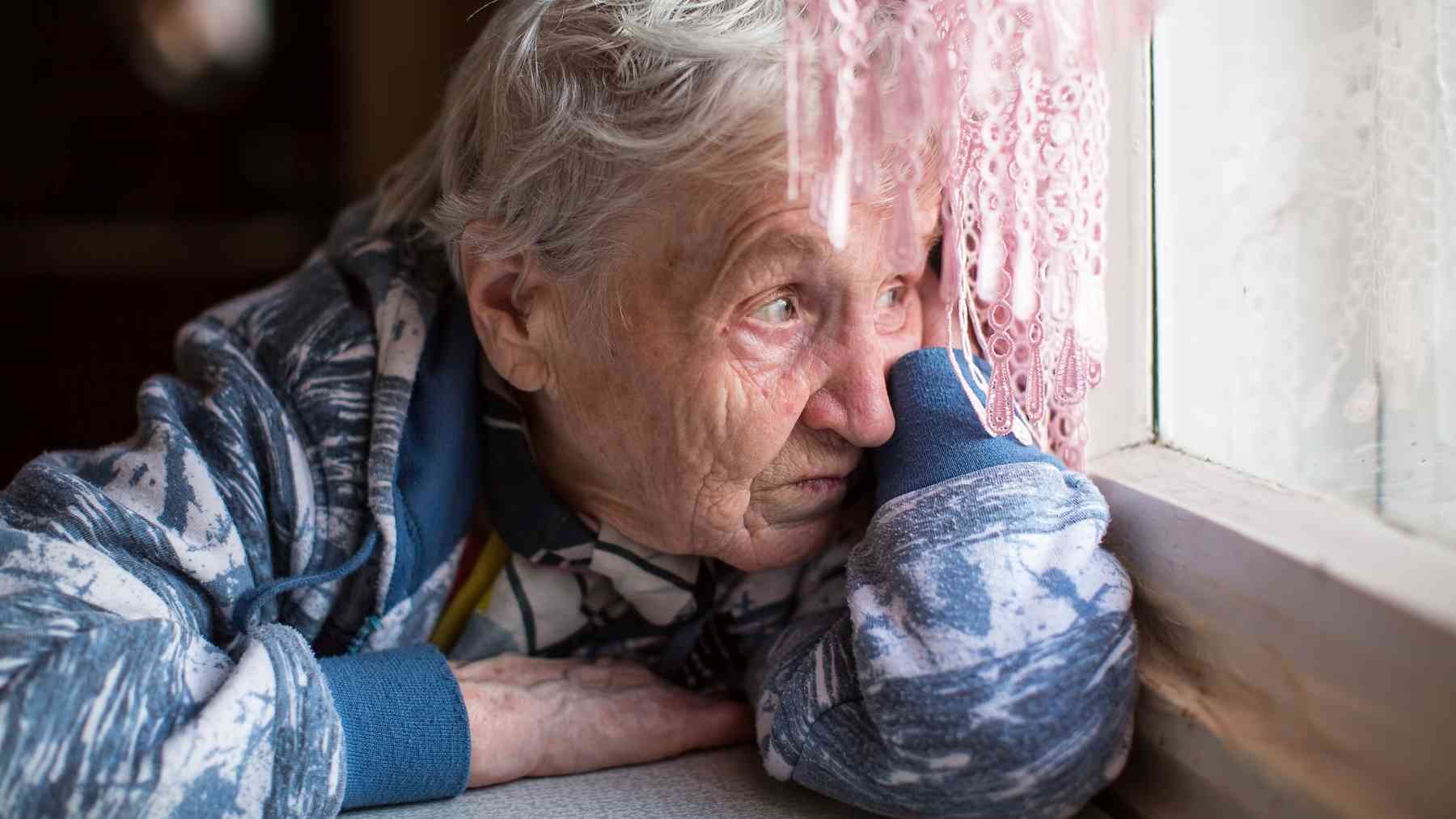 Older woman sitting alone by a window reflecting on loneliness and social isolation in old age