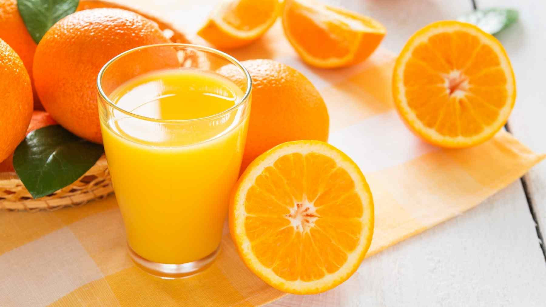 A glass of orange juice beside fresh oranges, illustrating a study comparing 100% orange juice with a sugary drink.