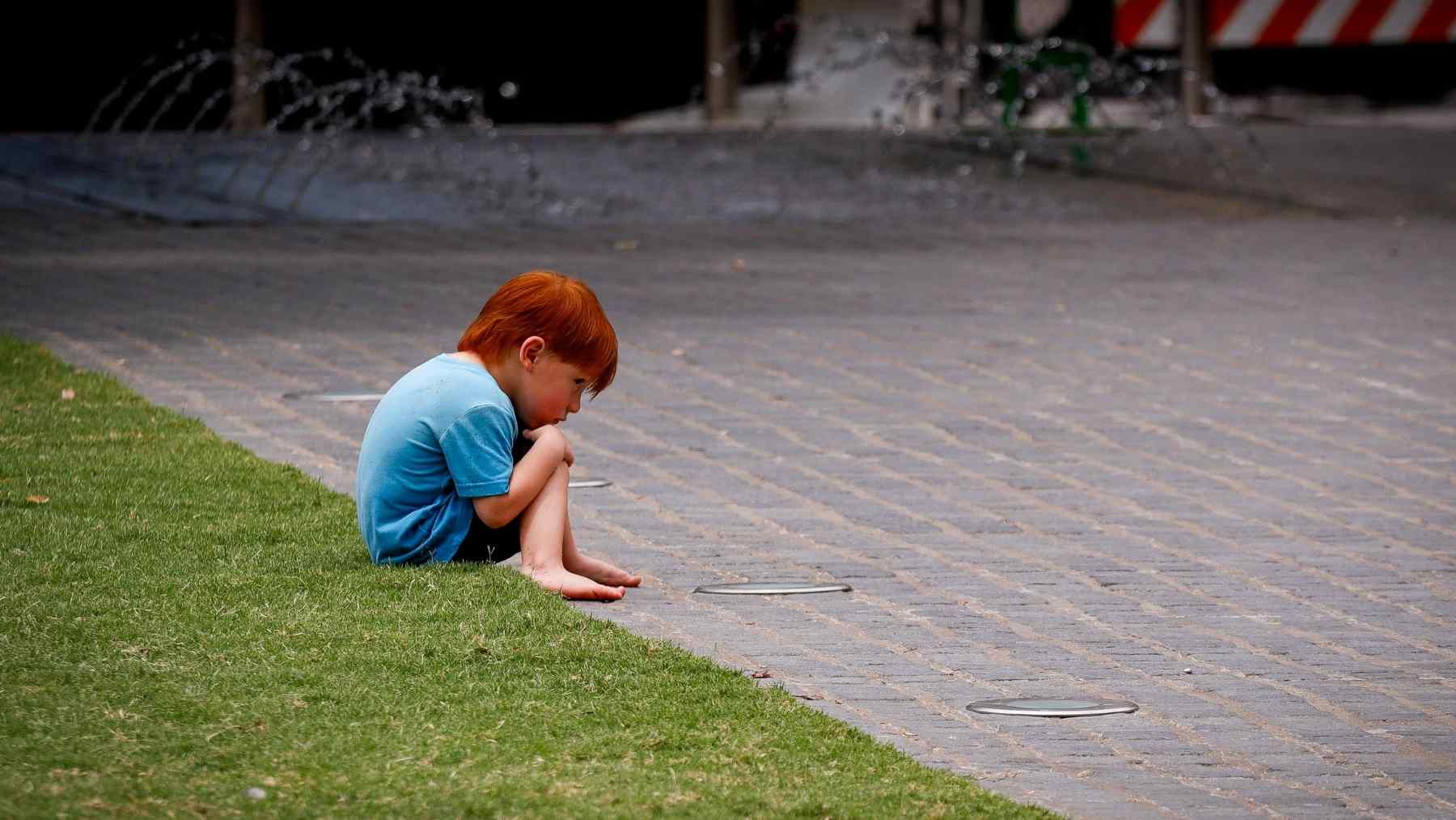 A young child sitting alone outdoors, reflecting the emotional distance linked to growing up with little praise