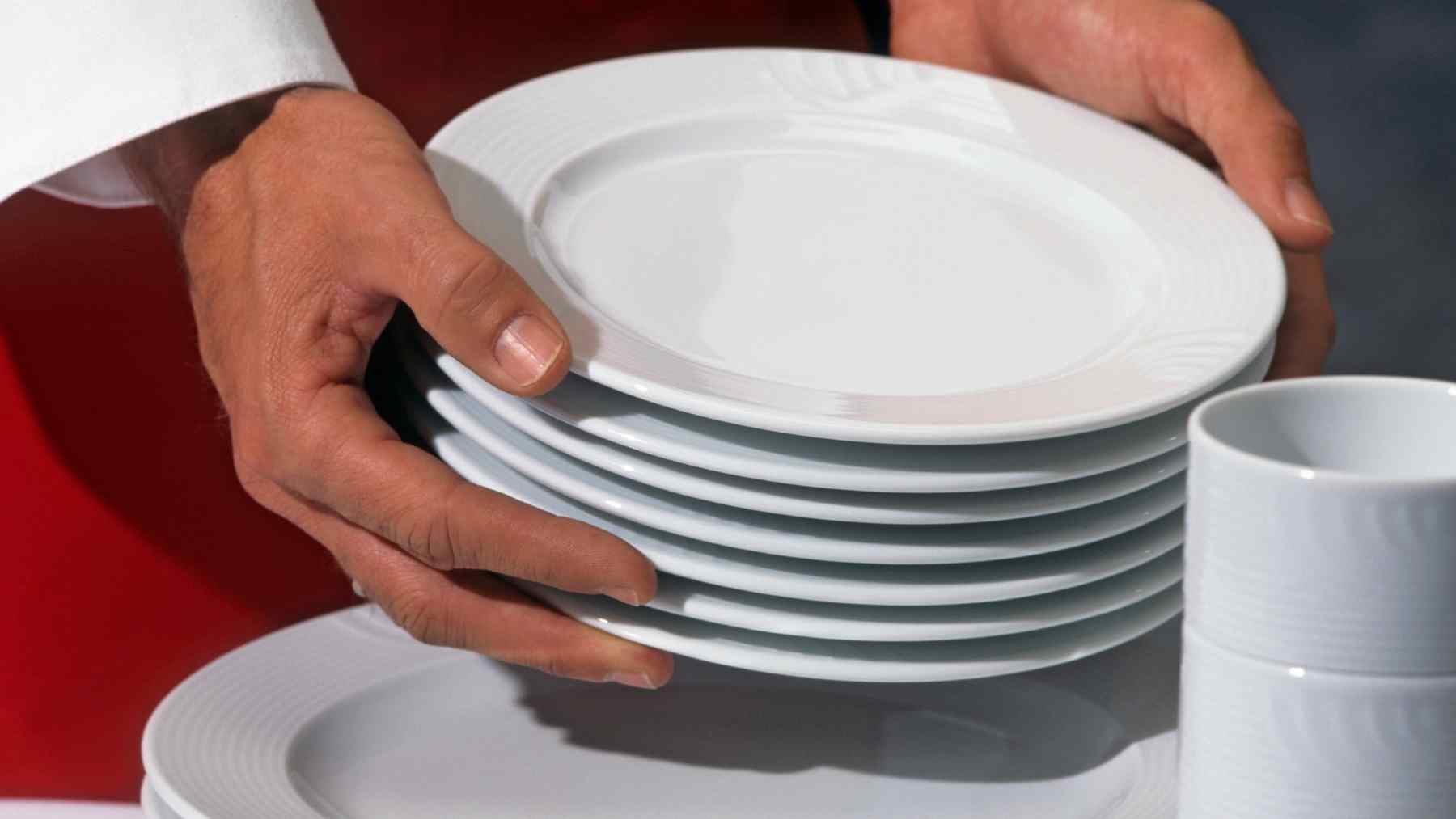 Hands holding stacked white plates at a restaurant after a meal, reflecting respect and consideration for servers.