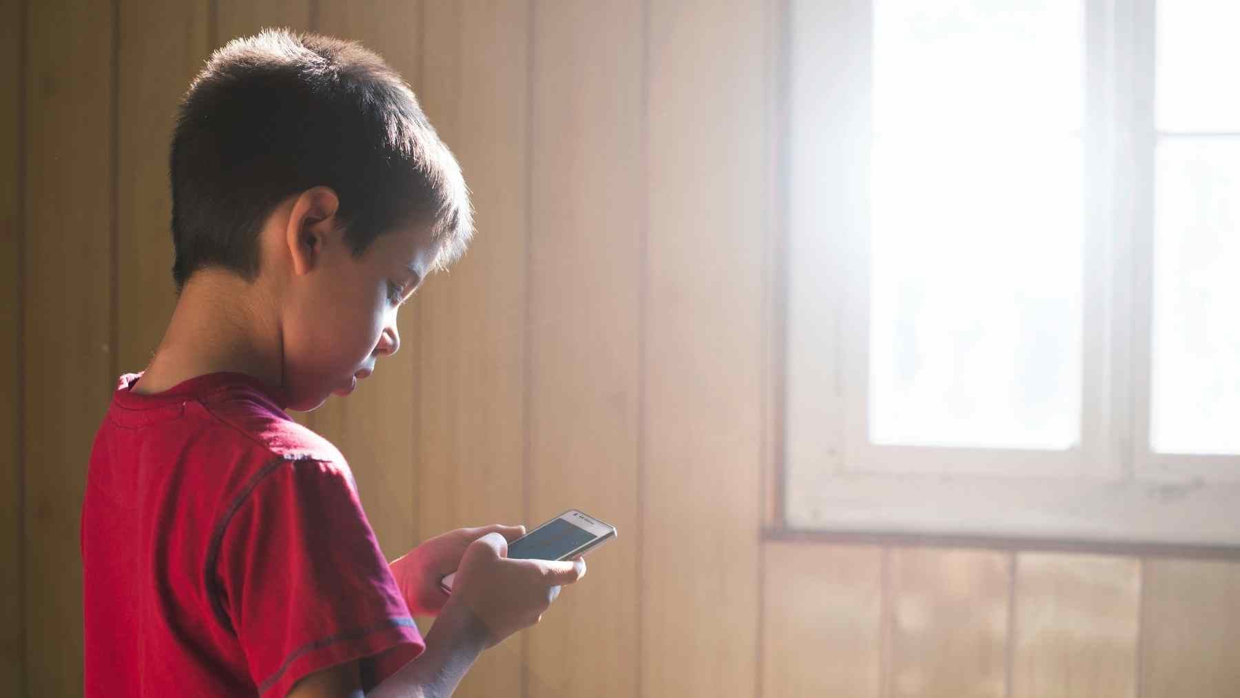 Young student looking at a cell phone indoors as schools restrict phone use over focus, anxiety, and social concerns