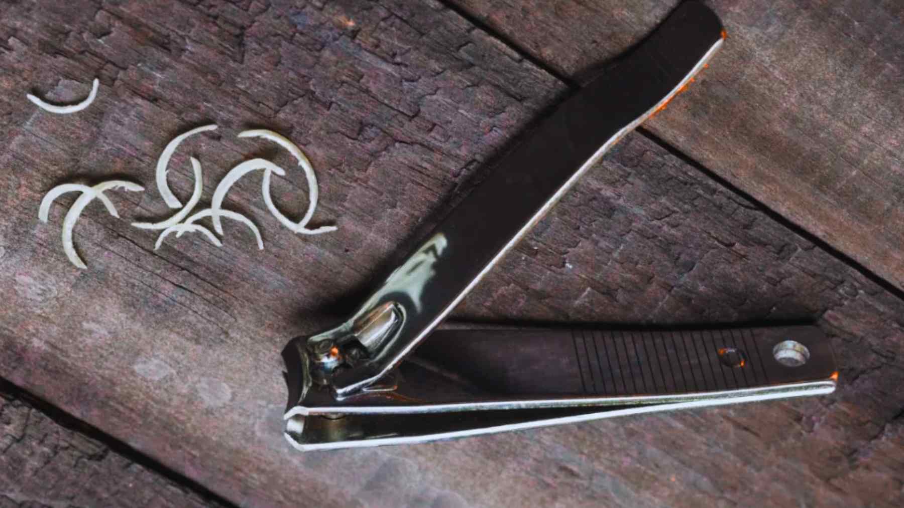 Metal nail clippers with the tiny hole in the handle shown next to fresh nail clippings