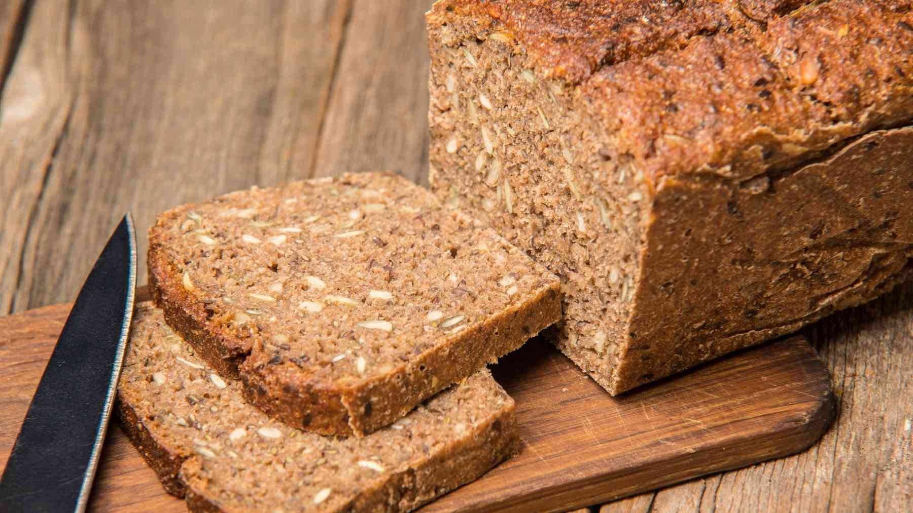 Sliced whole-grain bread on a wooden board, used to explain why it is not much lower in calories than white bread.