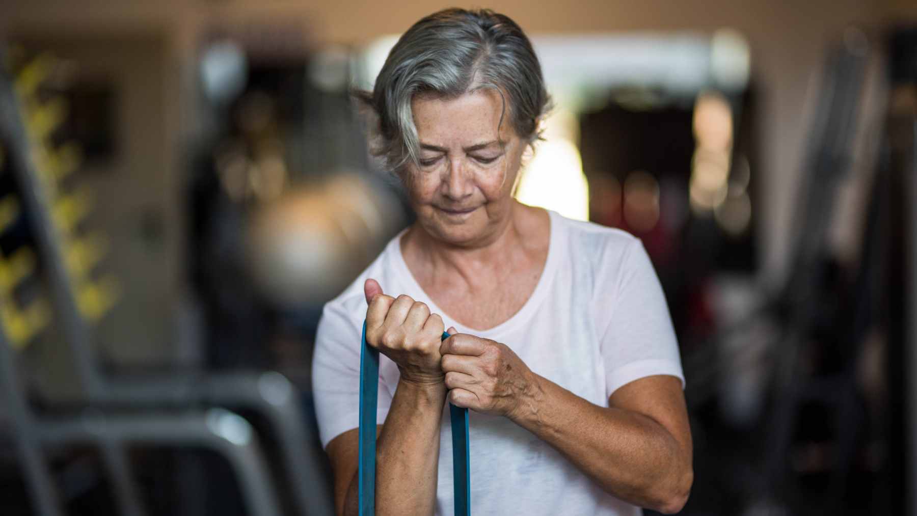 A 76-year-old woman confidently lifting dumbbells during a strength training workout in a bright, modern fitness studio.