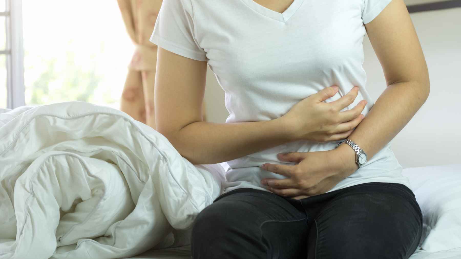 Young adult experiencing abdominal discomfort, highlighting constipation as a possible warning sign of colon cancer.