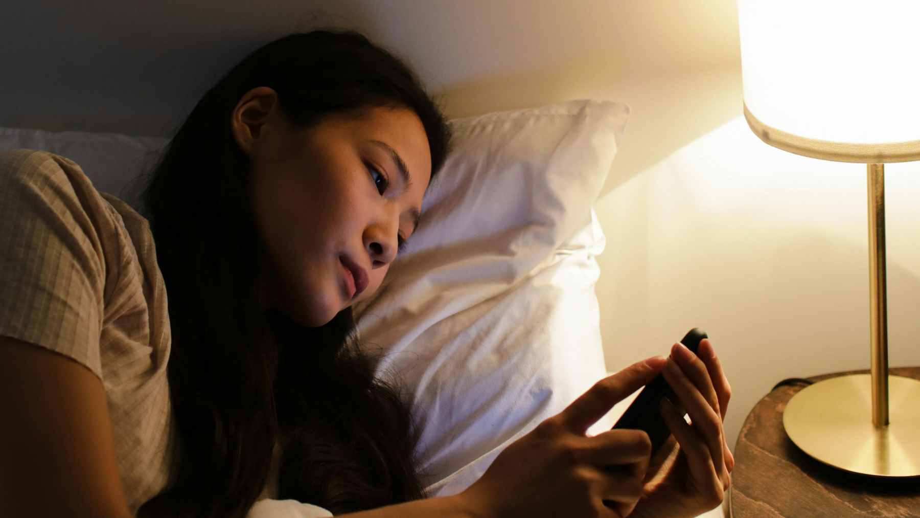 A person sitting in bed at night scrolling on their smartphone, which is disrupting their sleep patterns and circadian rhythm.