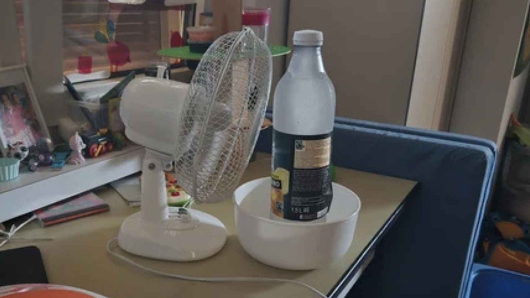 Frozen plastic bottle in a bowl placed in front of a small fan to create a simple cooling effect for sleeping during a heat wave.
