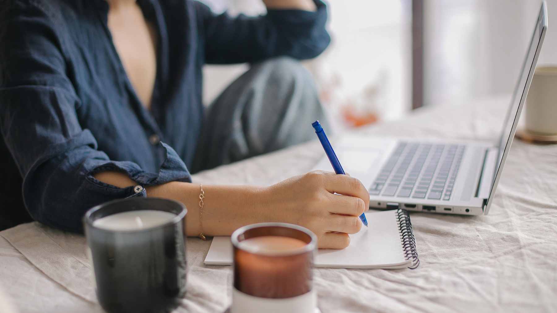 Psychology says people who take notes by hand in meetings aren’t old-fashioned, they’re doing something a lot of people don’t know how to do anymore 1 A close-up view of a person taking handwritten meeting notes in a notebook, surrounded by blurred office technology.