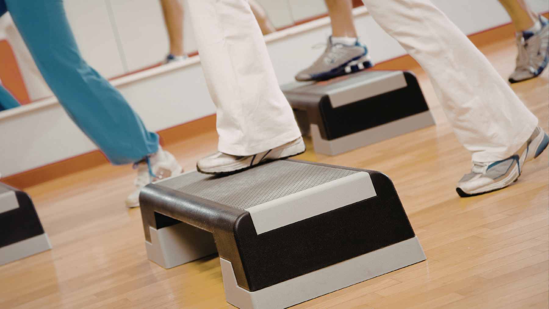 An older adult performing controlled step-up exercises near a sturdy support for balance and safety.
