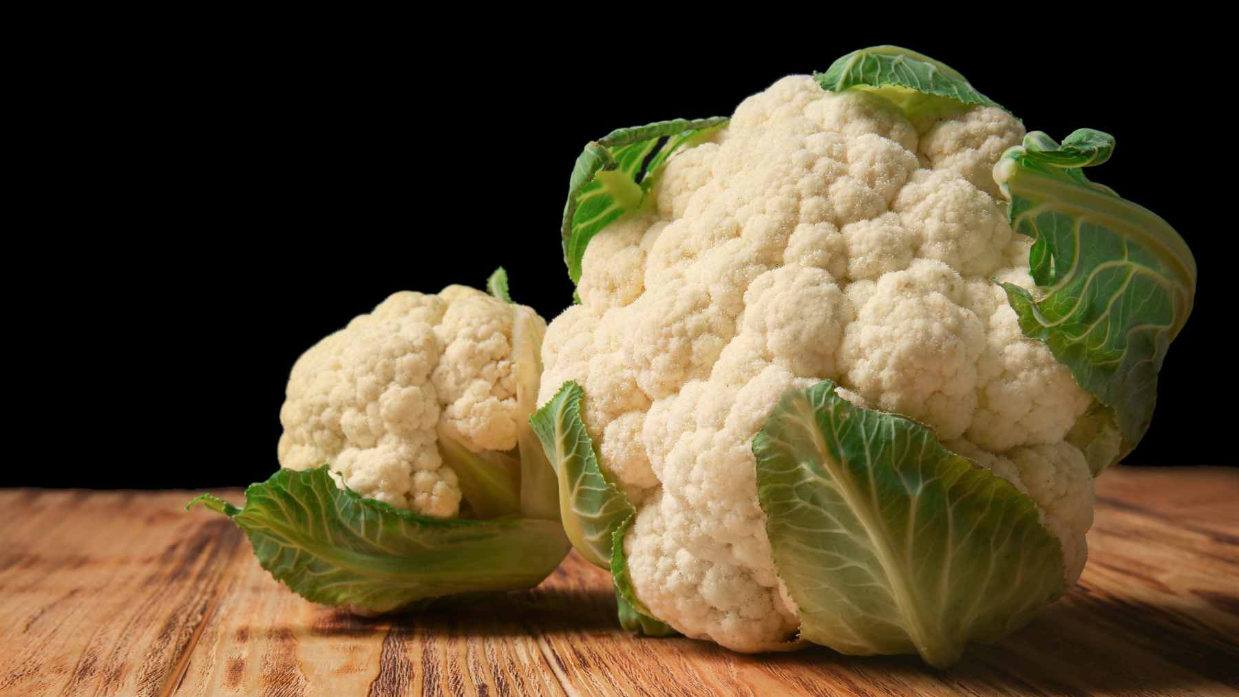 A whole tender cauliflower topped with creamy white sauce, crispy bacon bits, and fresh parsley, served as a classic Danish comfort dish.