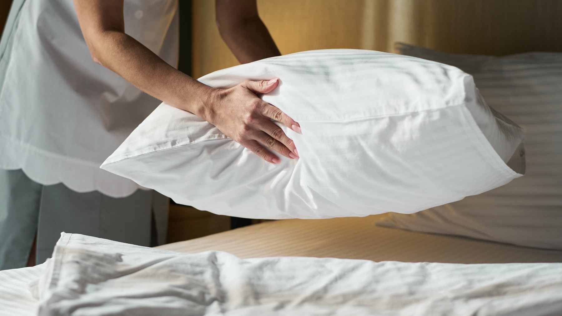 A person tidying their bed covers in a bright, modern bedroom during the early morning.