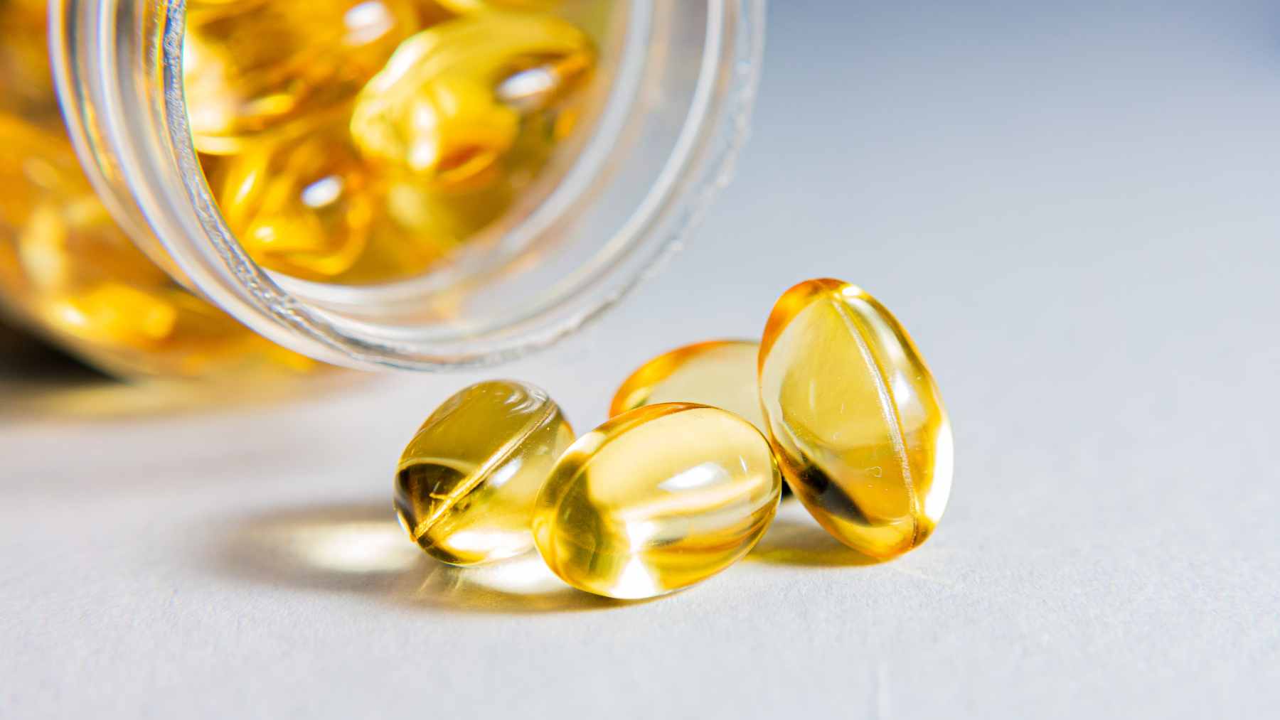 An older adult looking thoughtful while considering a variety of health supplements, including omega-3 fish oil capsules.
