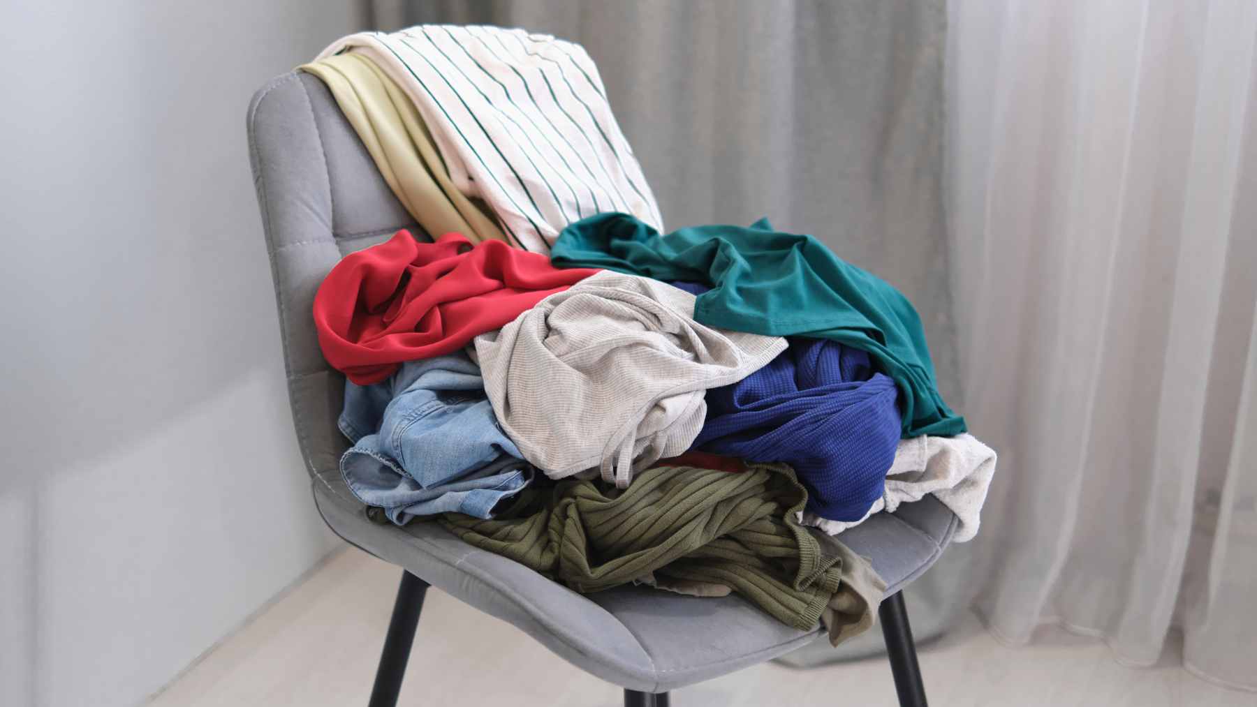 A bedroom chair piled high with various articles of clothing, illustrating the common "worn once" laundry habit.