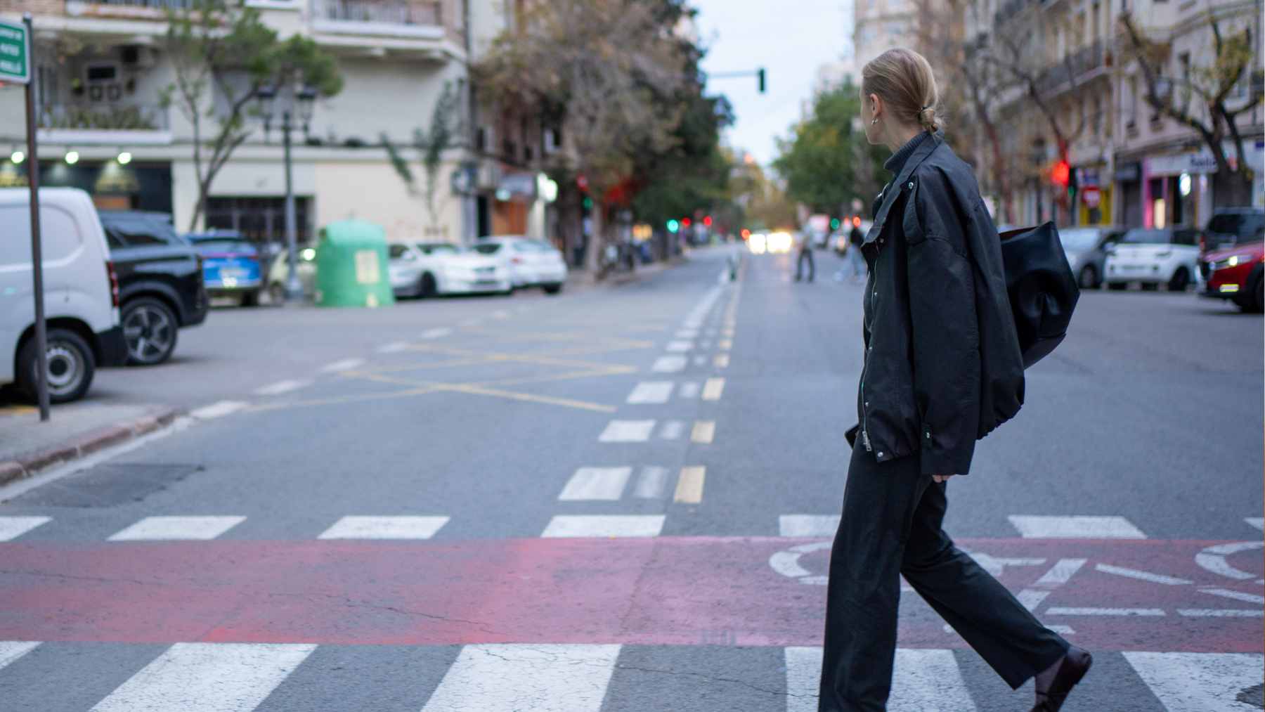 A pedestrian offering a friendly hand wave to a driver while crossing a busy city street.