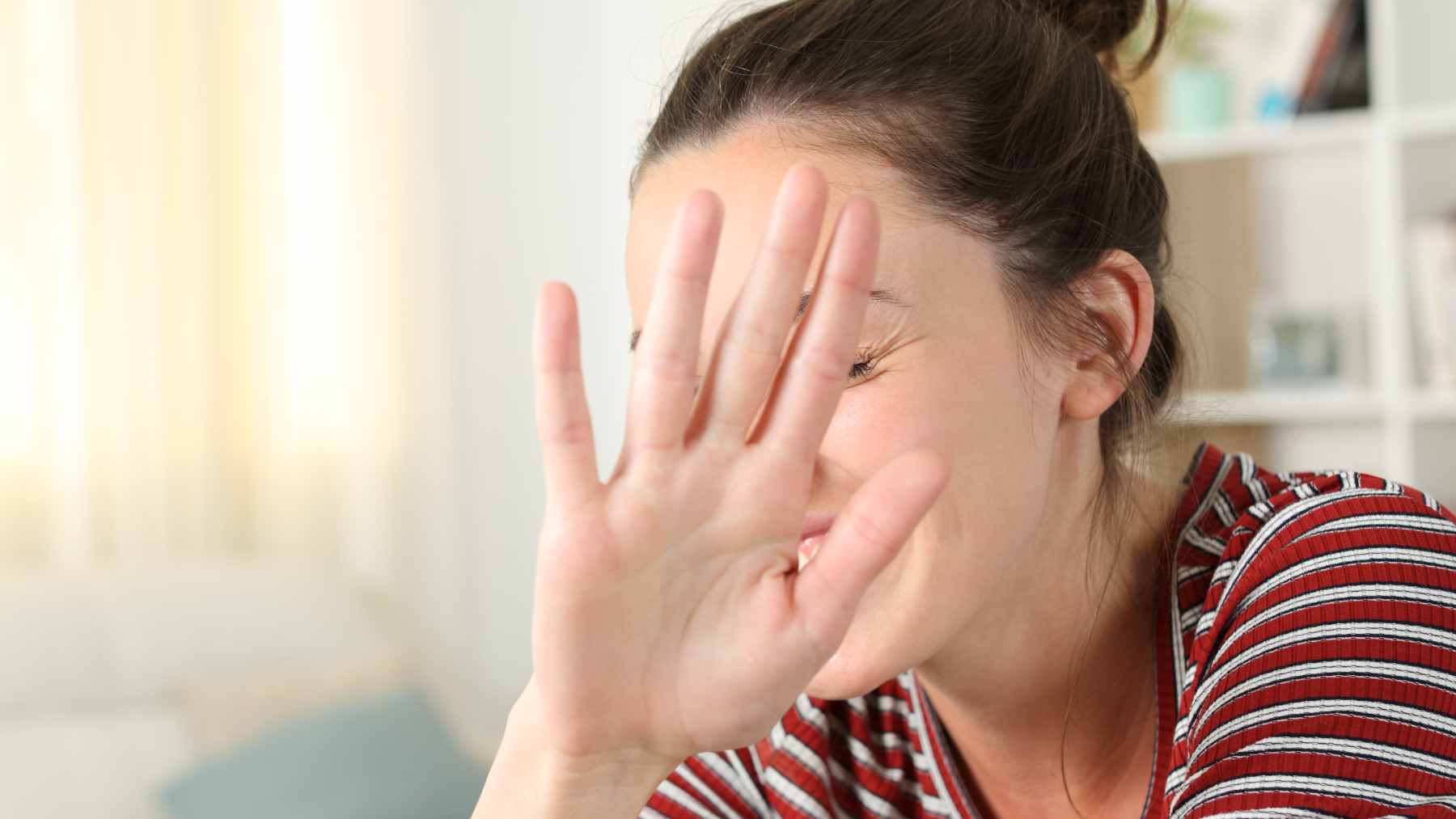 : A person shyly shielding their face from a camera at a social gathering, illustrating common feelings of self-consciousness.