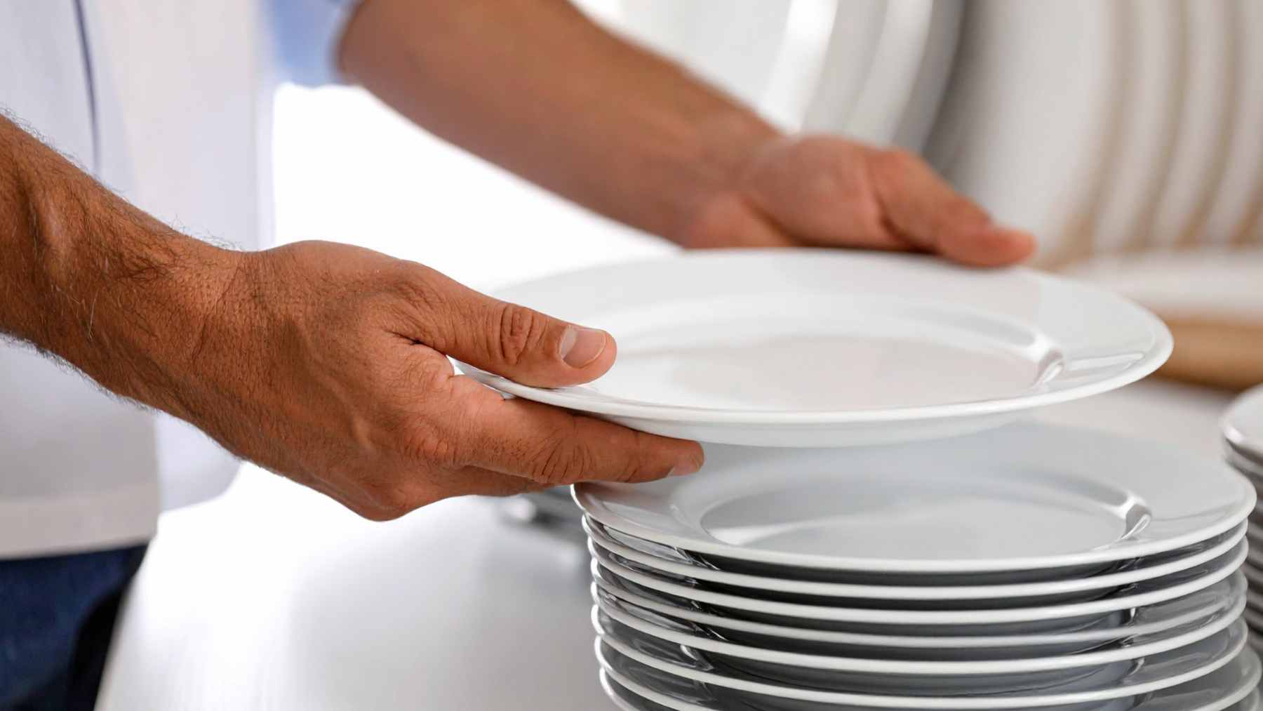 A customer stacking empty plates and glasses at a restaurant table to assist the server with cleanup.